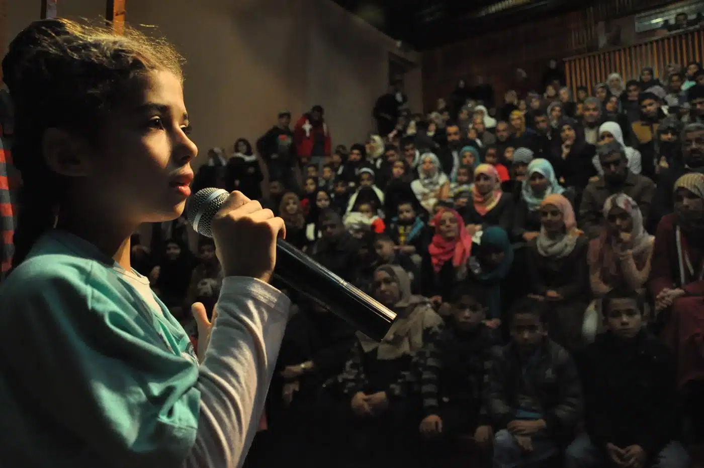 Een meisje spreekt met een microfoon een volle zaal toe tijdens het dramafestival van Theatre Day Productions in Rafah